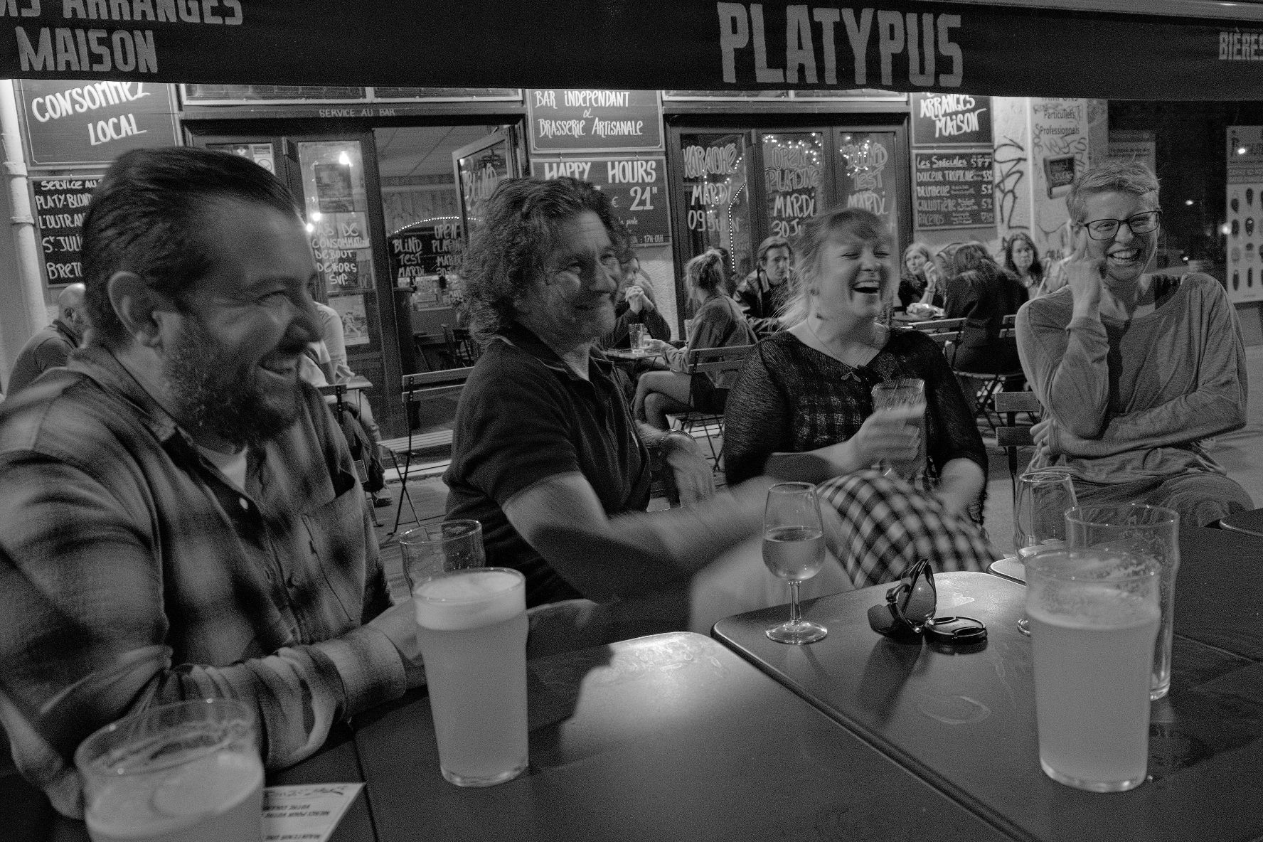 A black and white photo of four researchers laughing in a cafe after work.